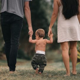 A male/female couple walks barefoot holding hands with a toddler