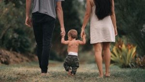 A male/female couple walks barefoot holding hands with a toddler