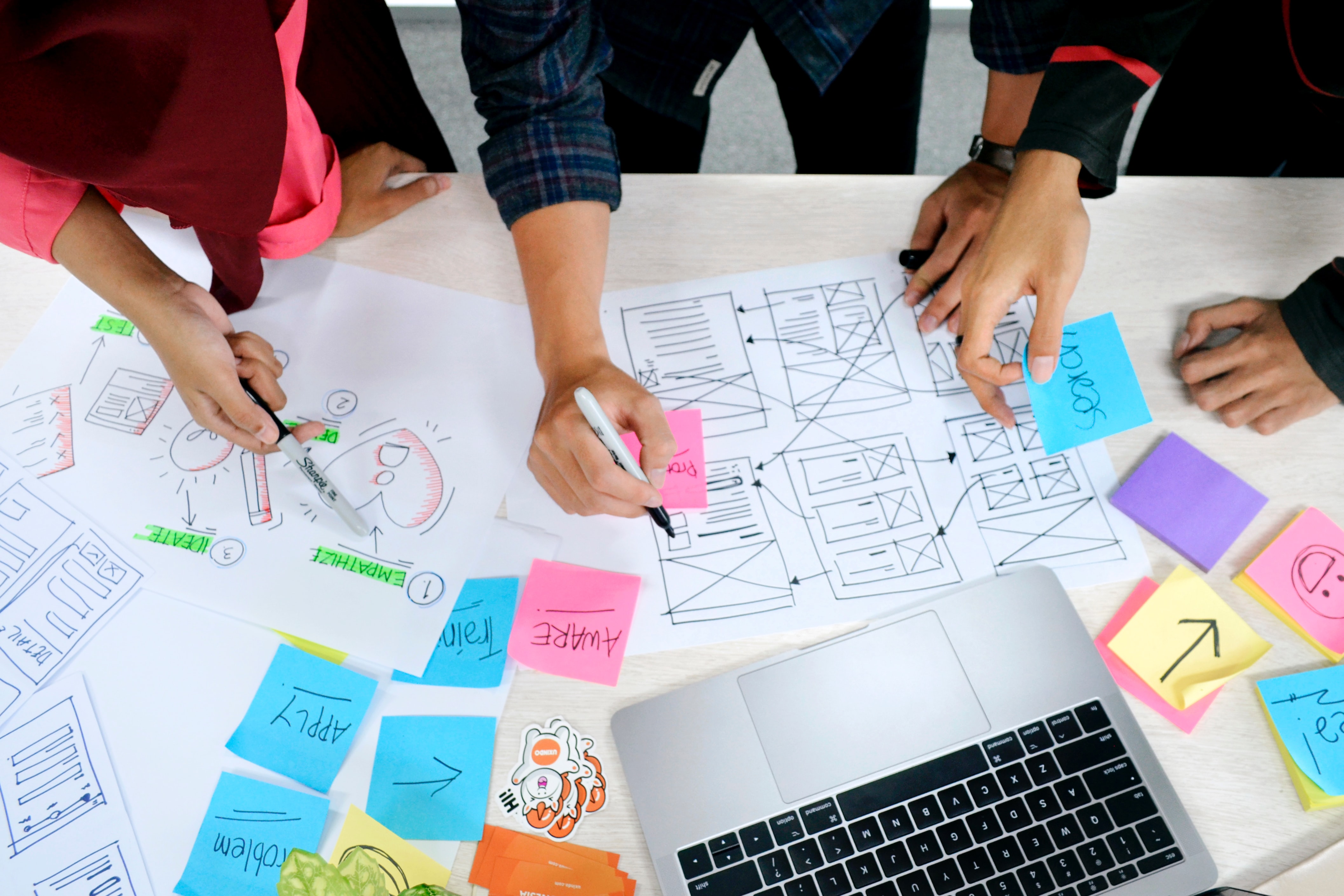 The hands of three or four people, many post it notes, a laptop, strategizing together