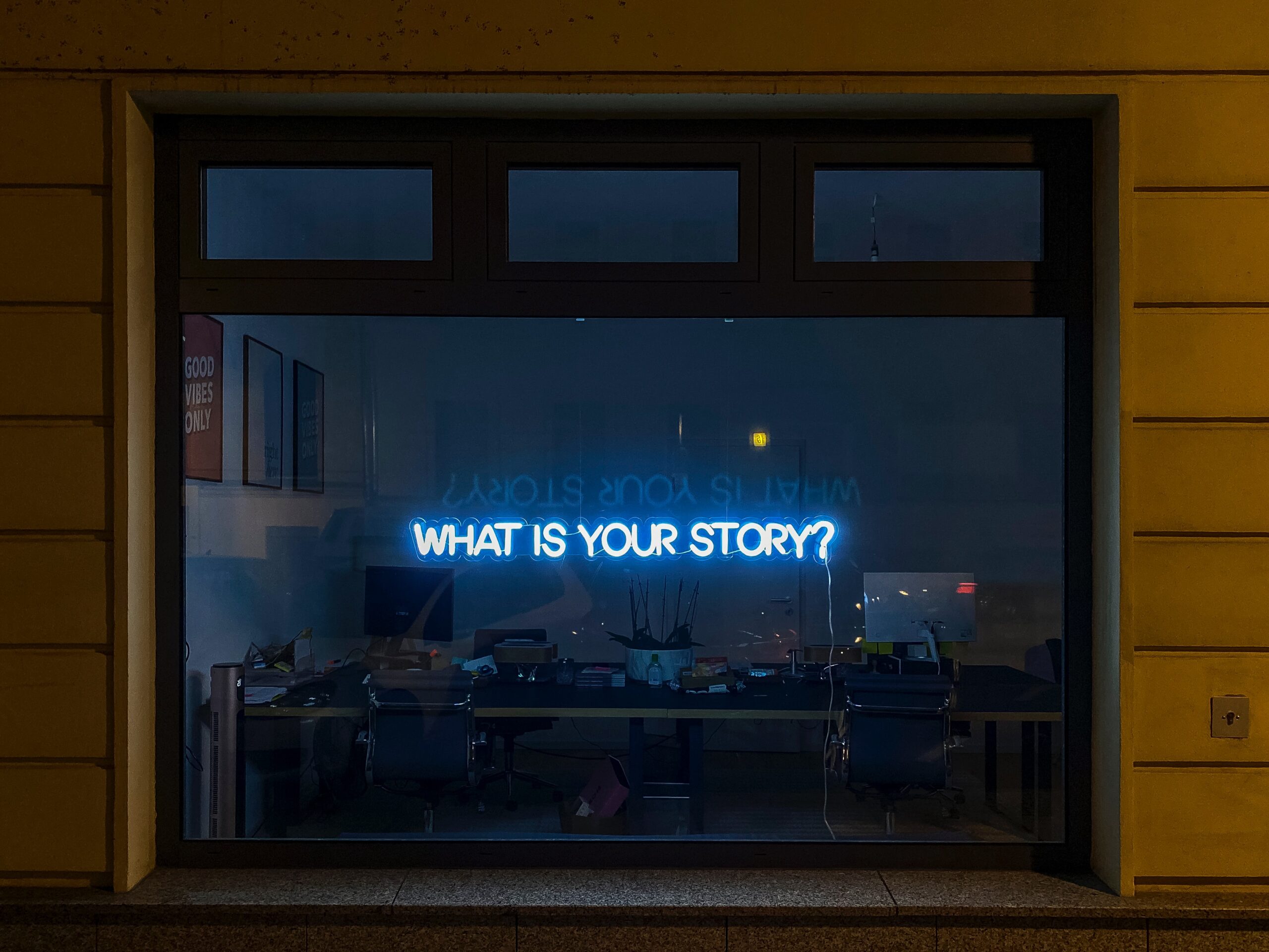 A window with a florescent sign: What is your story?